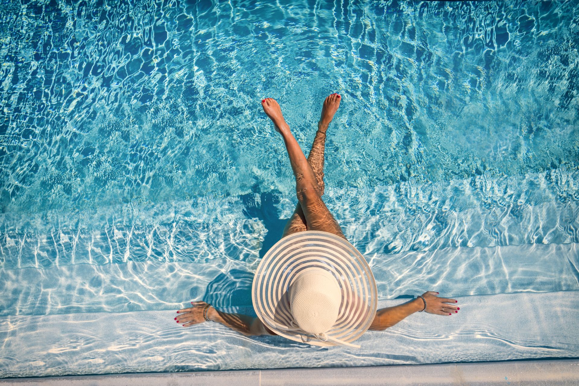 Frau mit Sonnenhut sitzt am Poolrand mit den Füßen im Salzwasser