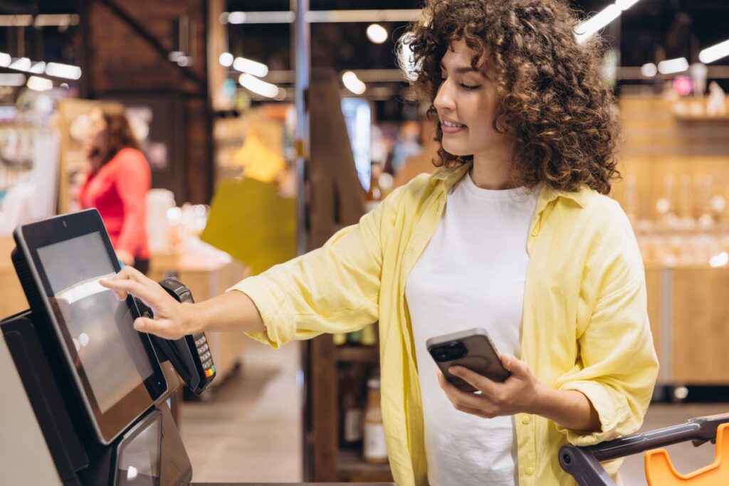 Frau nutzt Self-Checkout-Terminal im Supermarkt – Technik und Raumkonzept mit integrierter Kuehlvitrine beeinflussen das Vertrauen